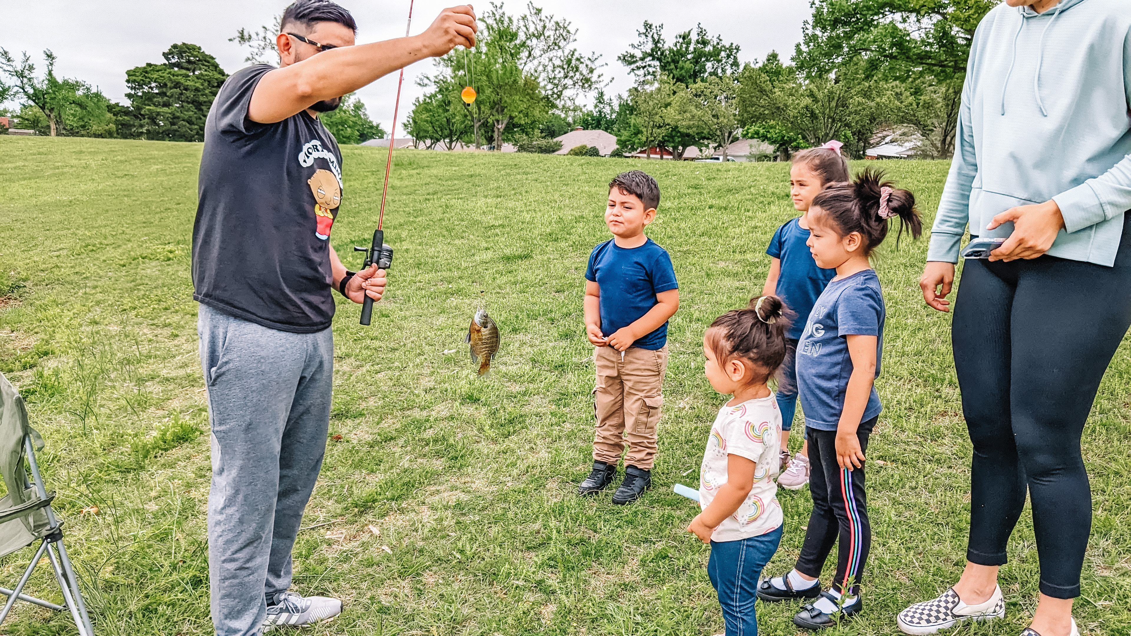 A person stands in front of a line of small children holding a fishing rod